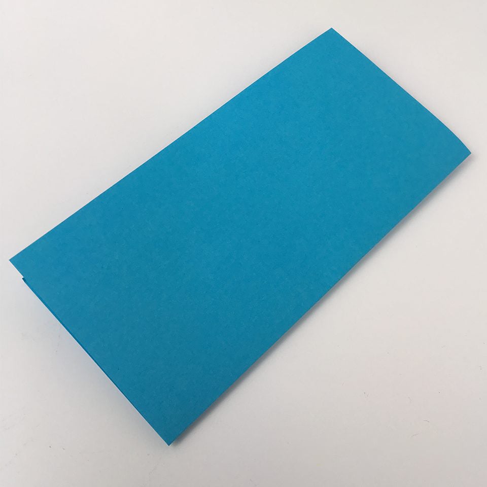 blue piece of paper folded in half as step one of making an origami box