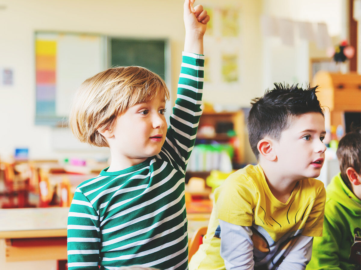 Young boy with hand up in classroom