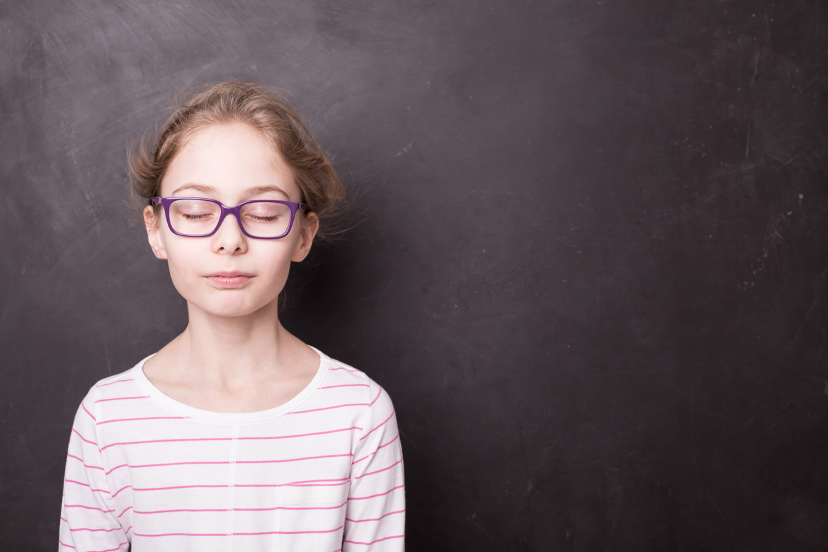 A girl stands in front of a blackboard with her eyes closed. Mindfulness in Education