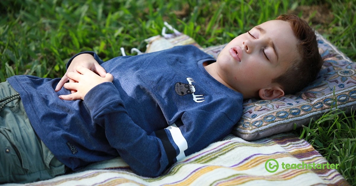 Boy laying on a blanket outside, with his eyes closed and hands on his belly
