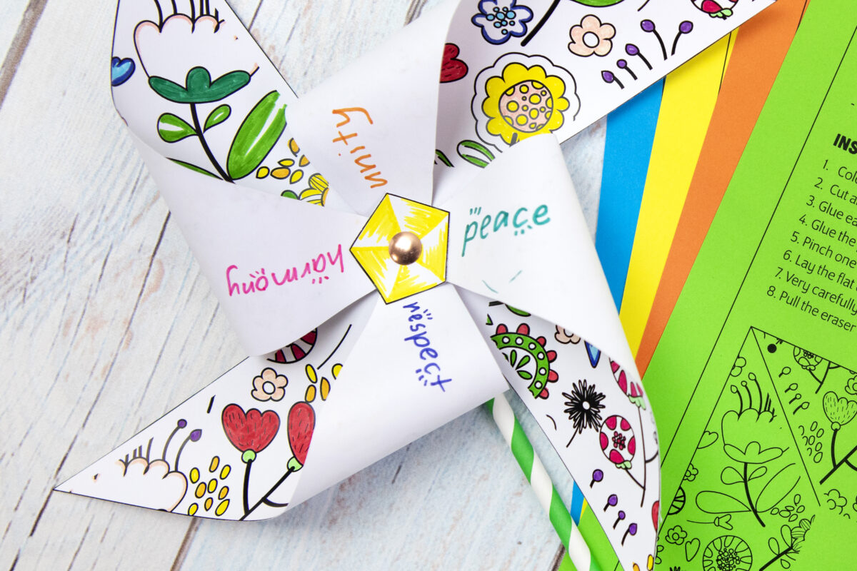 paper pinwheel with peace day words written on it sitting beside colored paper with paper pinwheel template