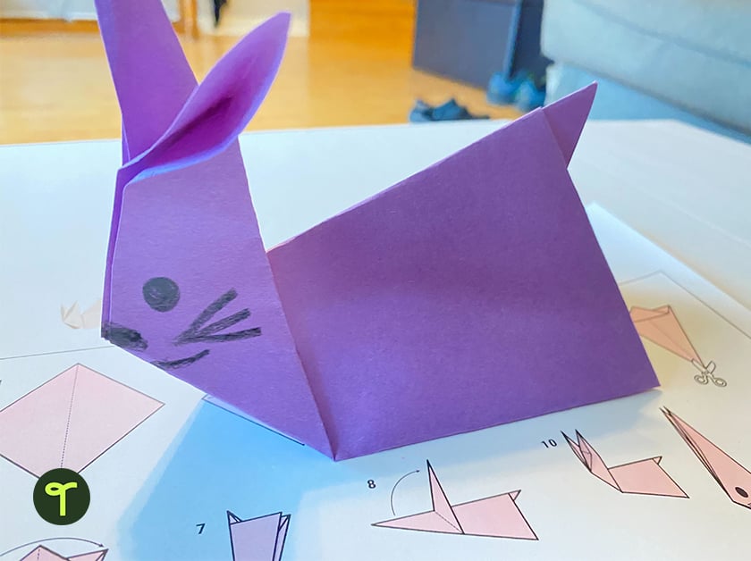 an origami bunny made using purple paper sits on top of an instruction sheet on a table