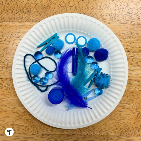A white paper plate on a wooden table with blue craft items on it