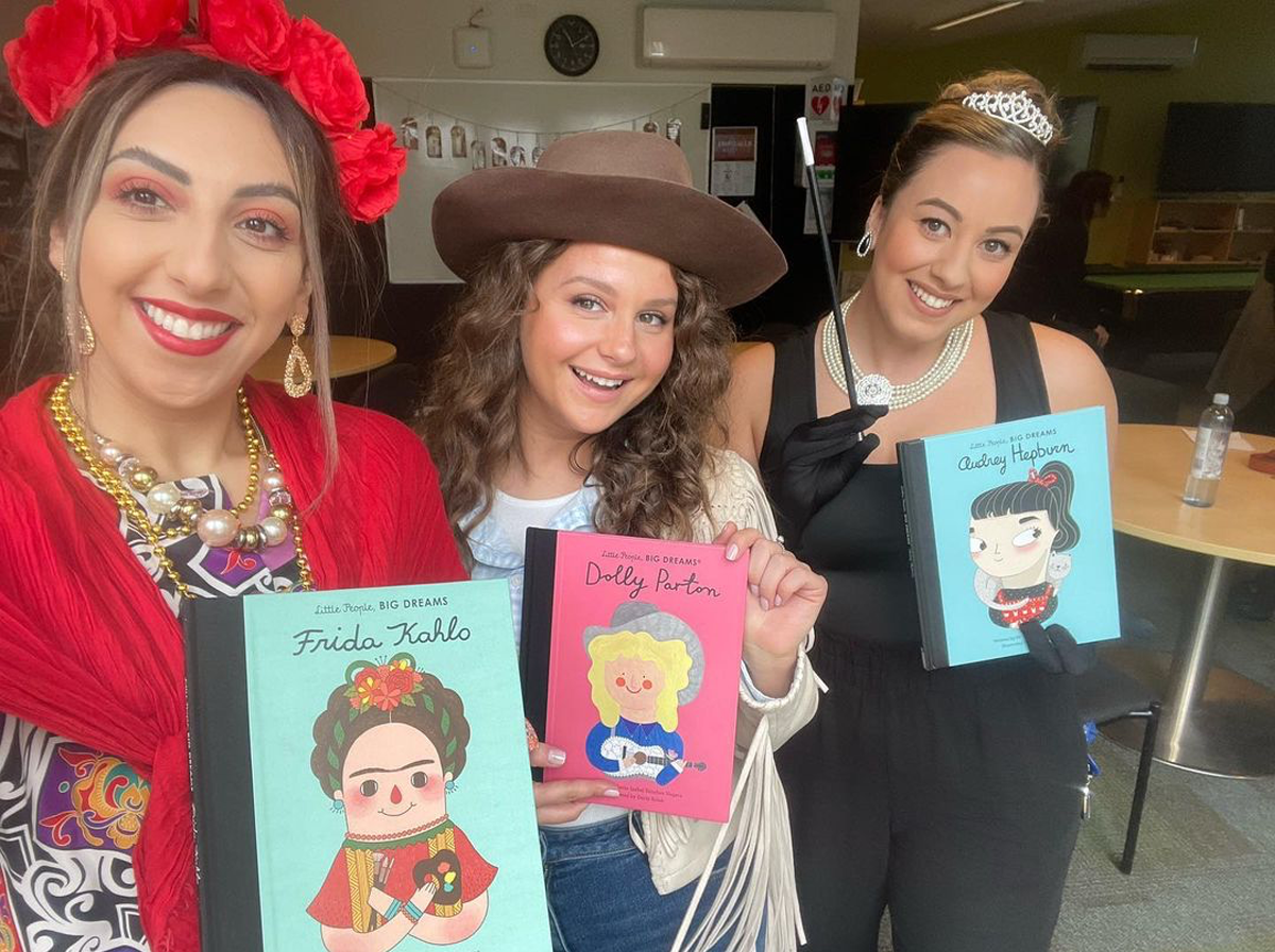 Three women in Book Week costumes holding kids books about Frida Kahlo, Dolly Parton and Audrey Hepburn.