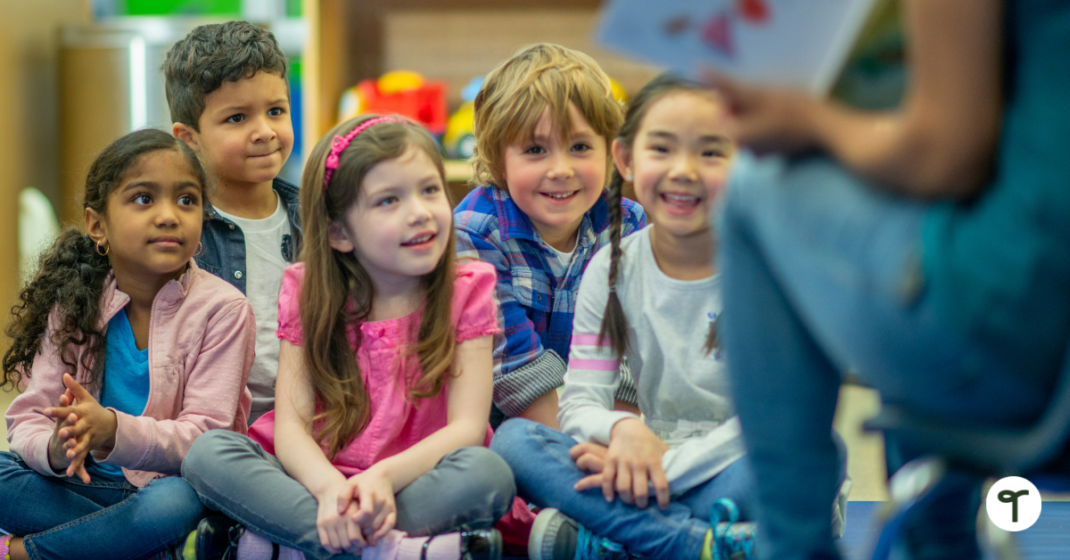 Elementary kids sitting on the floor listening to teacher reading a book.