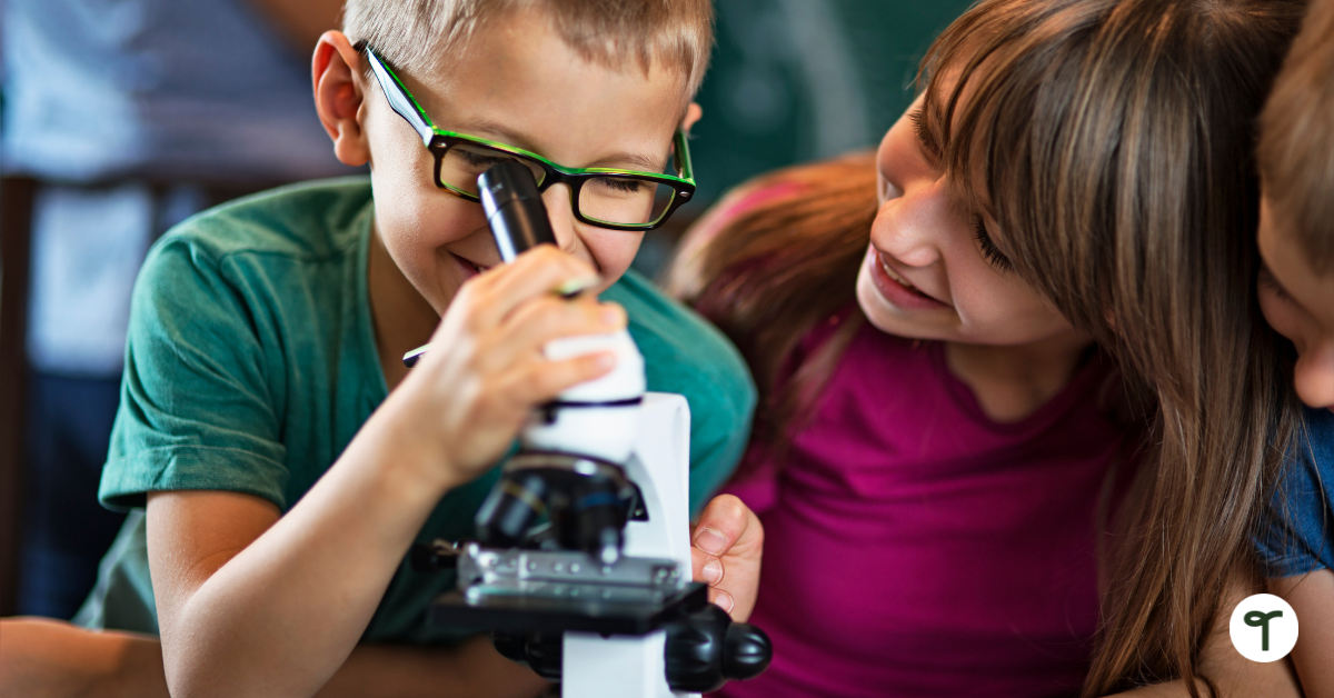 Student with glasses looking through microscope with classmate looking at him.