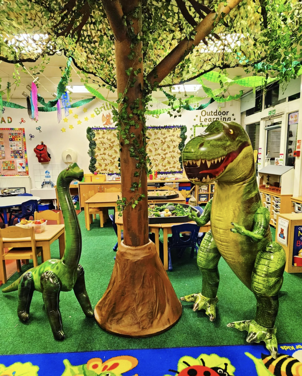 Classroom filled with plant decor and two inflatable dinosaurs in the foreground.