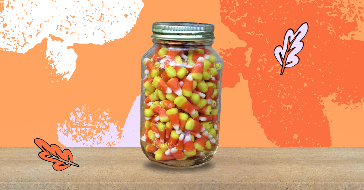 Candy corn in a jar on a table with an orange background.