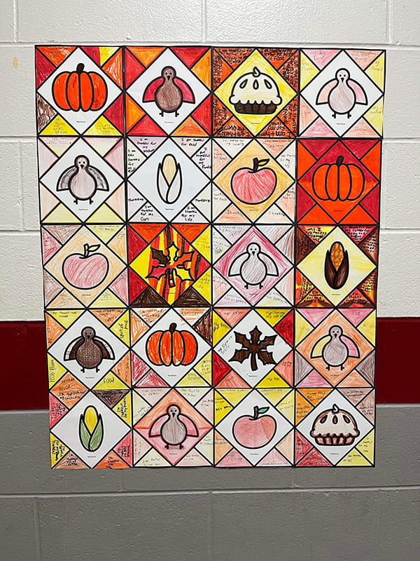 a thanksgiving bulletin board made of student artwork hangs on a wall in a school hallway