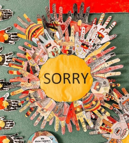 A yellow circle with the word 'sorry' in the centre, surrounded by paper handprints showing First Nations colours and symbols.