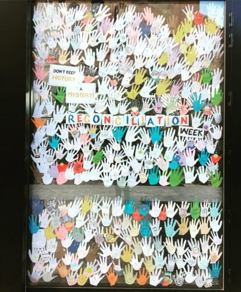 A classroom window display for National Reconciliation Week with paper handprints with First Nations colours and symboles
